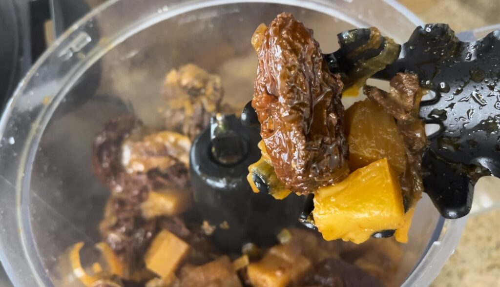 close up of slotted spoon with cooked pineapple chunks, onions and chipotle peppers being added to food processor