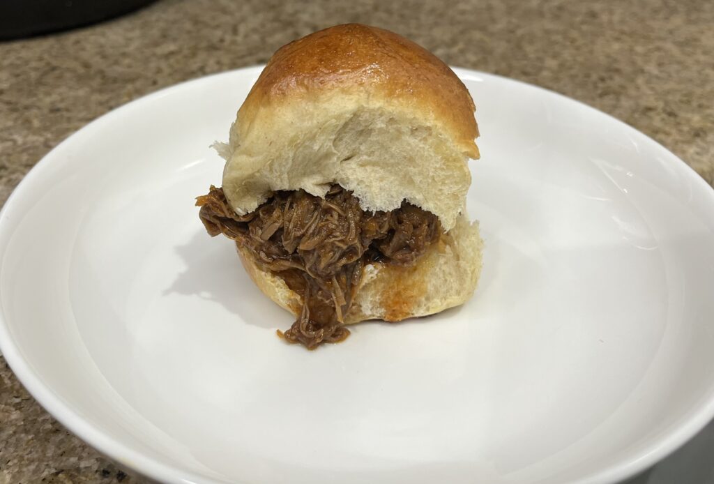 shredded chipotle chuck roast inside of a sourdough dinner roll dripping sauce down the front