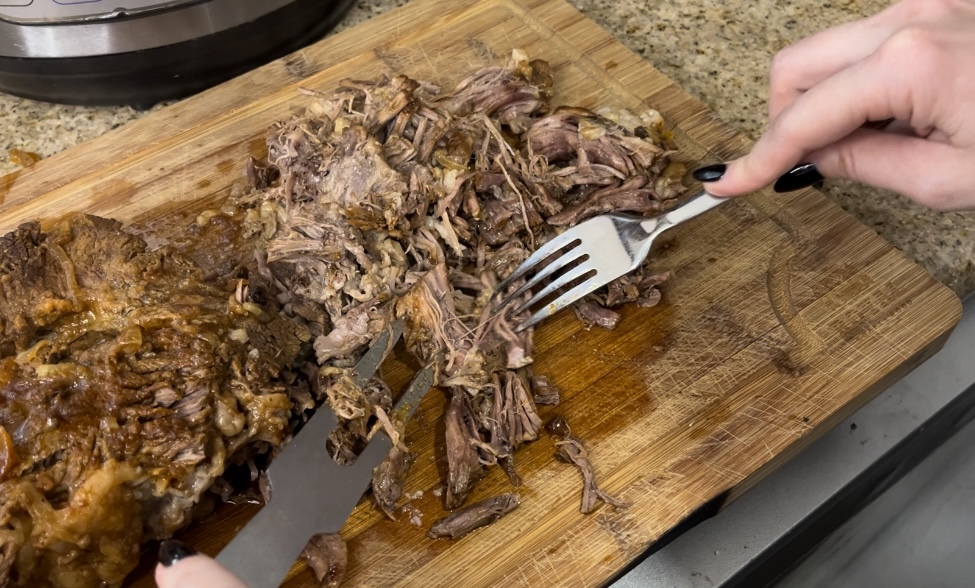 close up of chuck roast being shredded with fork on cutting board