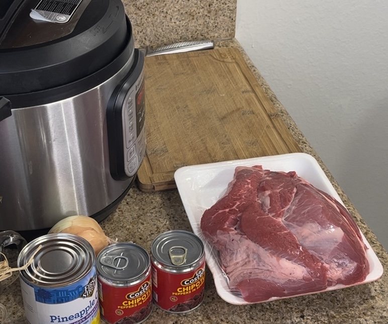 onions, canned pineapple, canned chipotle peppers, package of raw chuck roast, cutting board and instant pot on a countertop