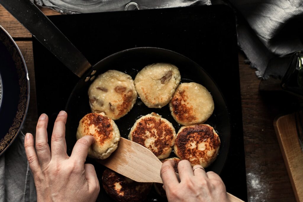 6 pancakes in a pan with hands and spatula flipping a pancake