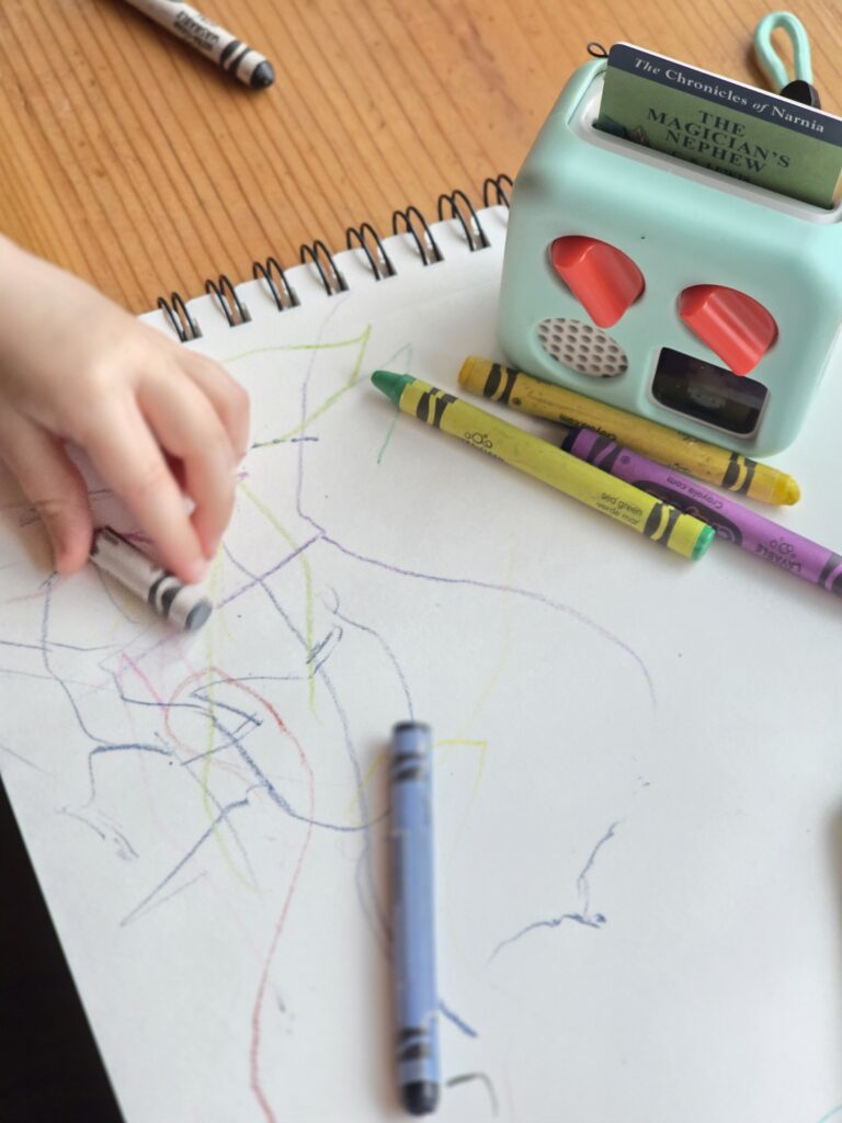 yoto player on top of sketchbook with crayons and baby hand coloring with a crayon
